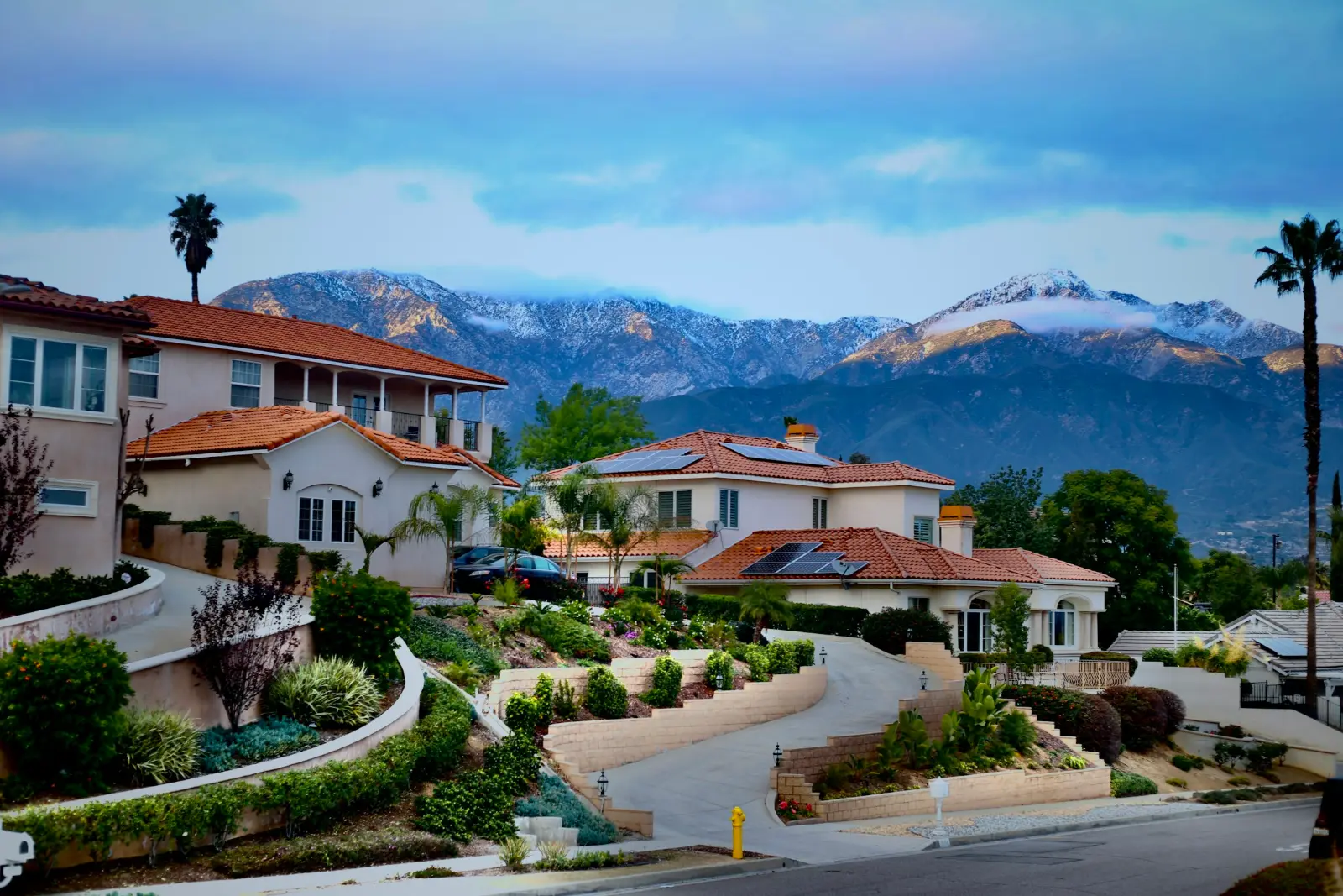 Residential hillside street with tile-roof homes and snow-capped mountains behind, in Upland, California